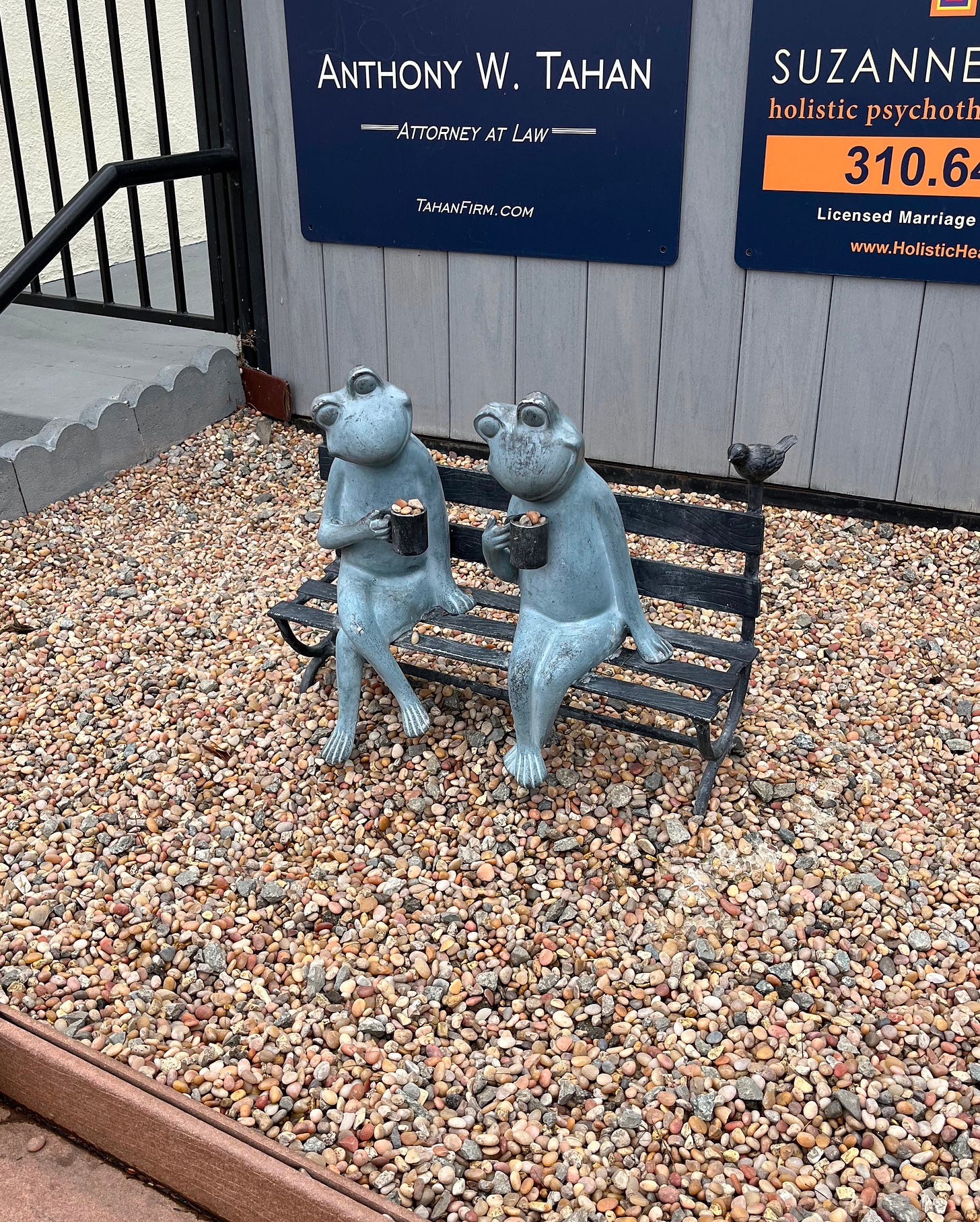A sculpture of two frogs sharing a cup of coffee on a bench.
