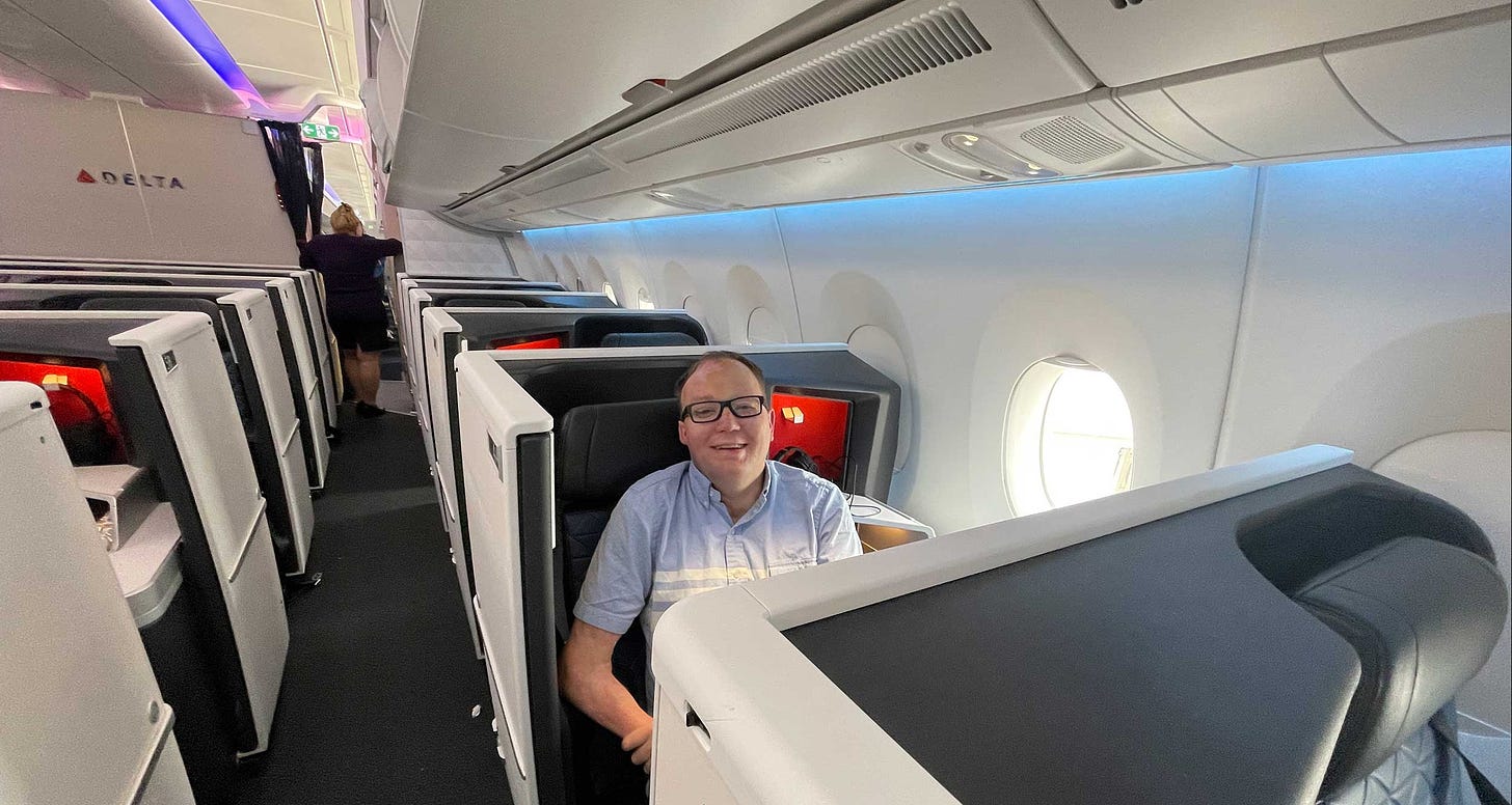 John pictured seated in business class seat by the window on a Delta aircraft.