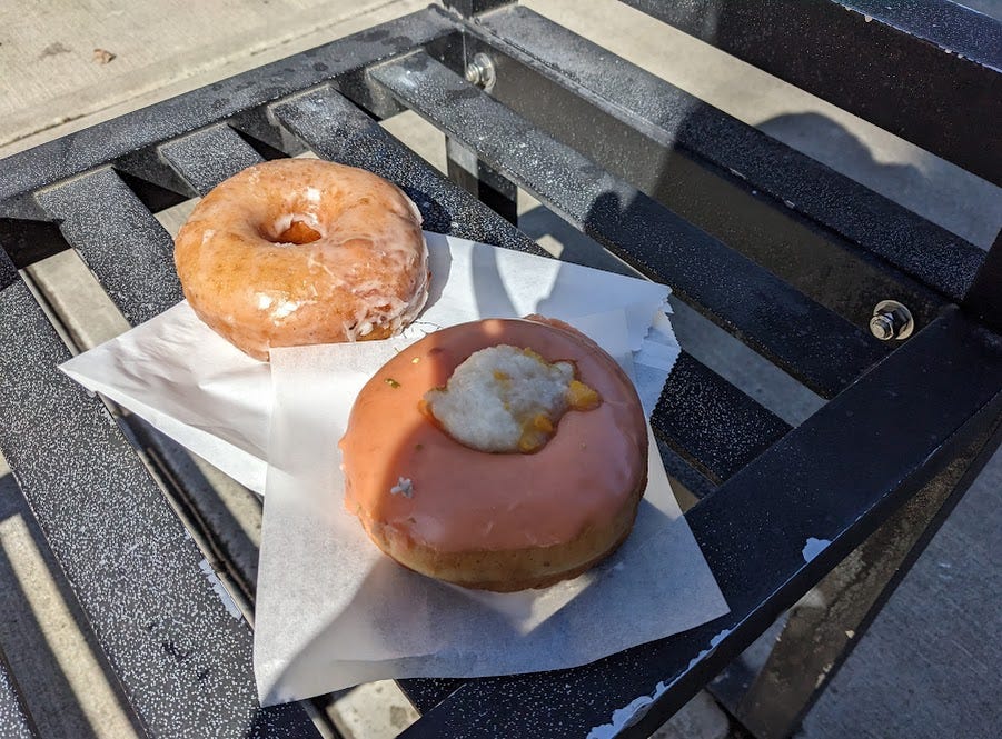 glazed vanilla bean doughnut and peaches and cream doughnut, sitting on a bench