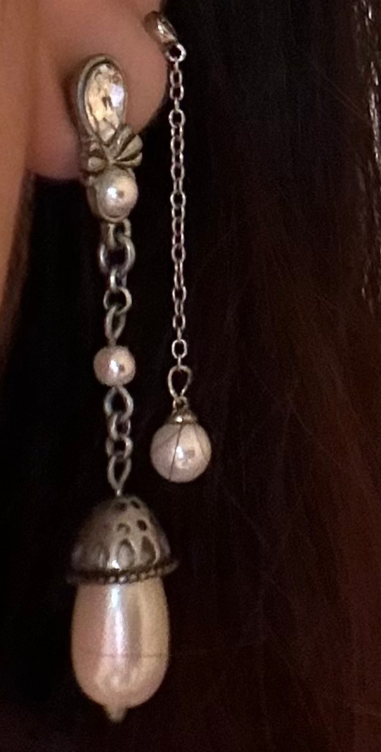 the bottom half of a white person's earlobe wearing silver dangling earrings with pearl embellishments in each of two piercings.