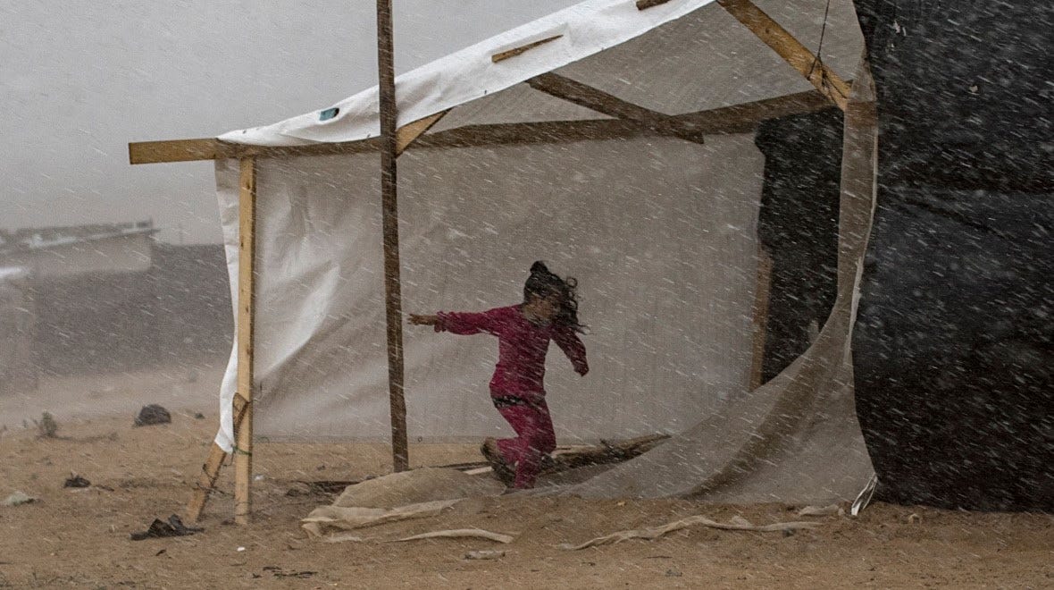 A young girl is running under a makeshift shelter as rain pours on a camp 