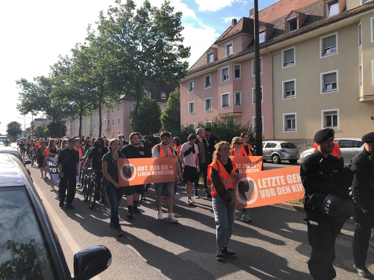 Bild 1: Menschen mit Bannern und Warnwesten laufen mit Begleitung der Polizei auf der Furtmayrstraße in Regensburg.