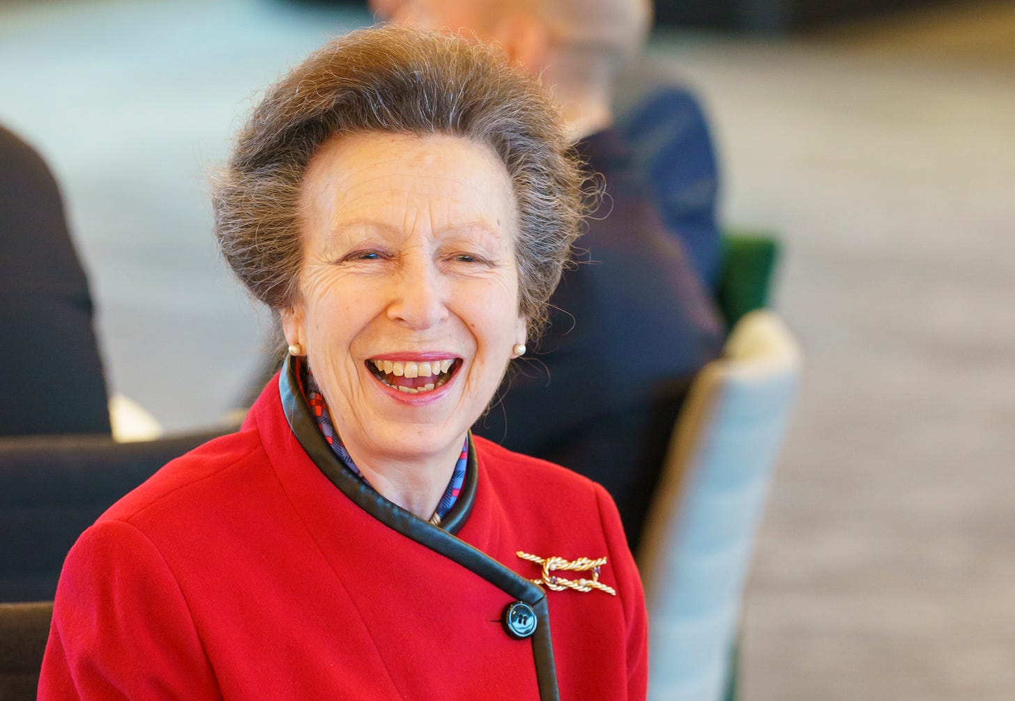Princess Anne smiling and wearing a red coat