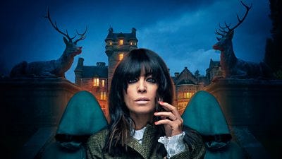 Claudia Winkleman stands outside a castle with two hooded figures behind her