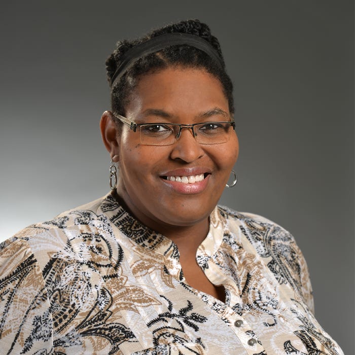 Studio portrait photo of Halcyon M. Lawrence, a smiling Black woman wearing glasses who is a Trinidadian academic researcher