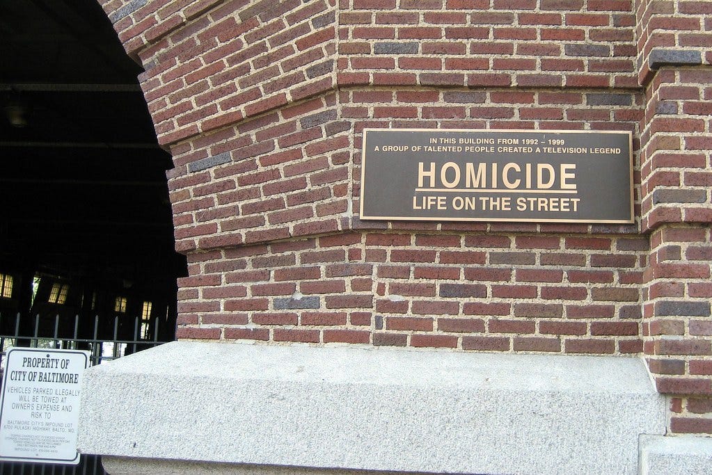 This image shows a sign once attached to the Broadway Pier Building in Baltimore’s Fells Point neighborhood that served as the exterior shooting location for Homicide: Life on the Street's Homicide Squad. The sign, in gold letters over a black background, reads, "In this building from 1992 to 1999 a group of talented people created a television legend--Homicide: Life on the Street." This image shows a sign once attached to the Broadway Pier Building in Baltimore’s Fells Point neighborhood that served as the exterior shooting location for Homicide: Life on the Street's Homicide Squad. The sign, in gold letters over a black background, reads, "In this building from 1992 to 1999 a group of talented people created a television legend--Homicide: Life on the Street."
