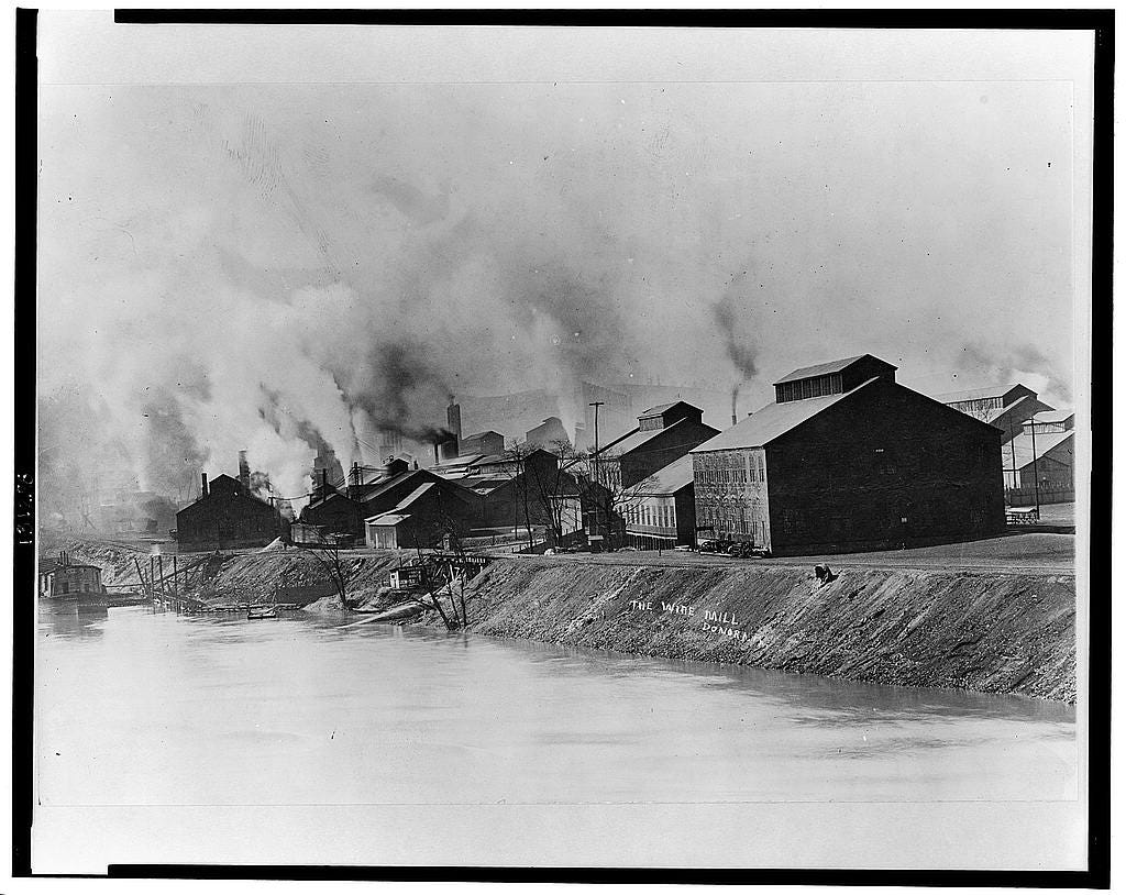 river on left, buildings with smokestacks belching smoke