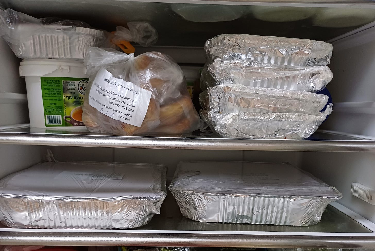 Shelves of refrigerator showing foil pans of food and a labeled sack of rolls to be given to soldiers for holiday and Sabbath meals.