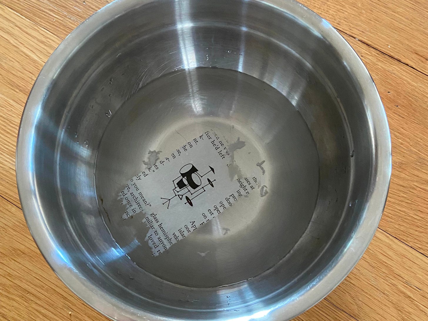 A bowl of water with a piece of tape with a bit of magazine stuck to it with an image of a drumset