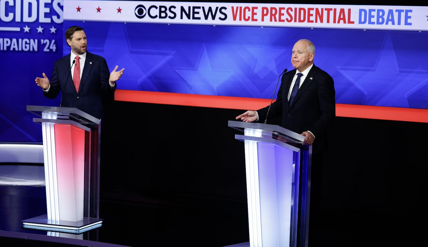 Two men in suits stand at lecterns in front of a screen that said 'CBS News Vice Presidential Debate'