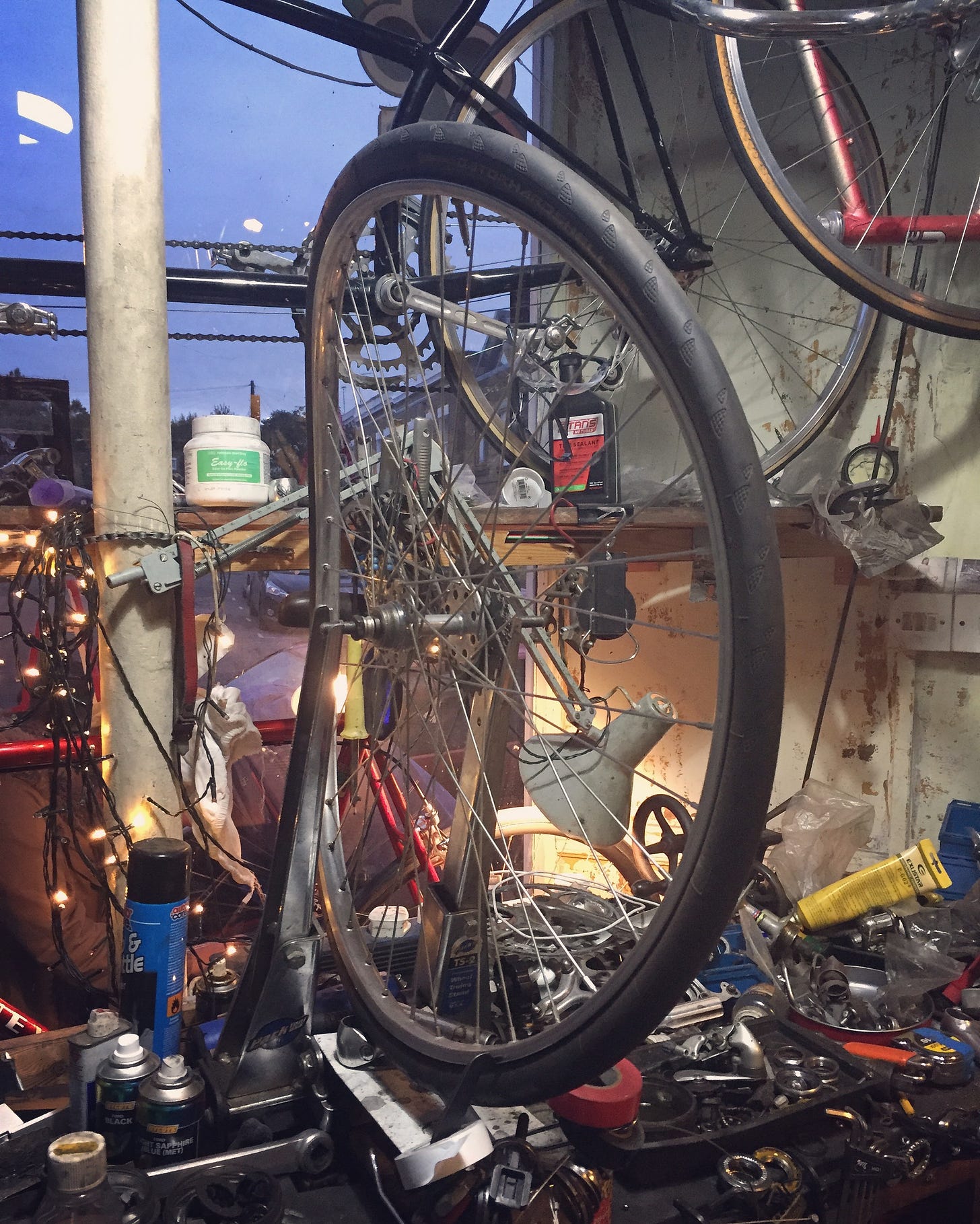 a very bent wheel sits in a truing stand in a messy bike workshop
