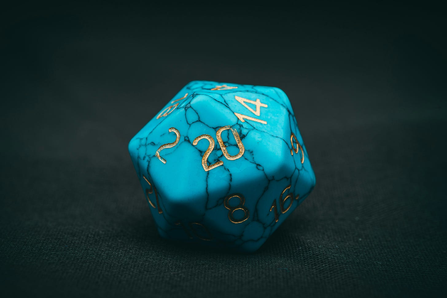 A turquoise twenty-sided die with gold lettering.