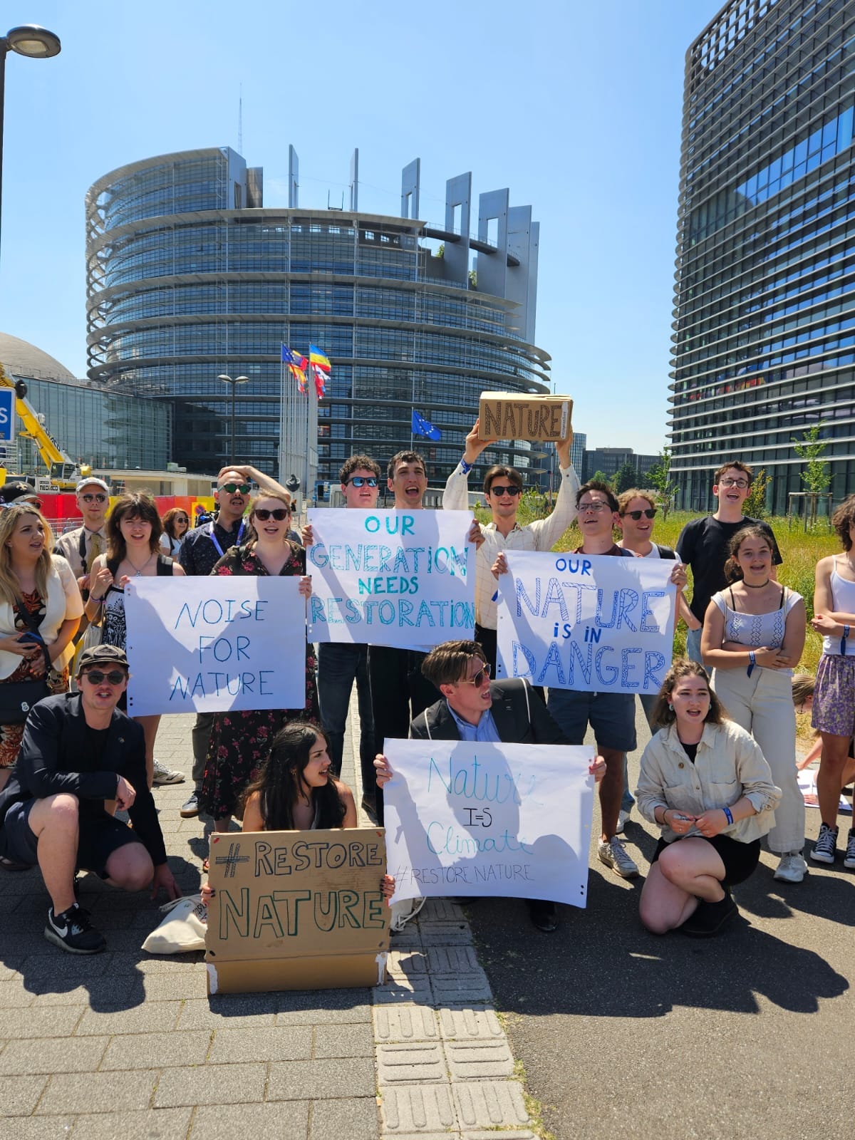 Group of around 20 youth activists hold signs that say 'noise for nature' and 'our nature is in danger' in front of the European Parliament in Strasbourg.