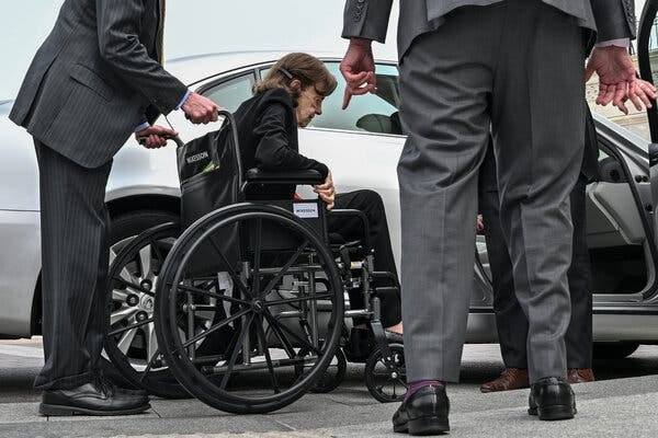 Senator Dianne Feinstein of California in a wheelchair near a car. She is wearing a dark suit. 