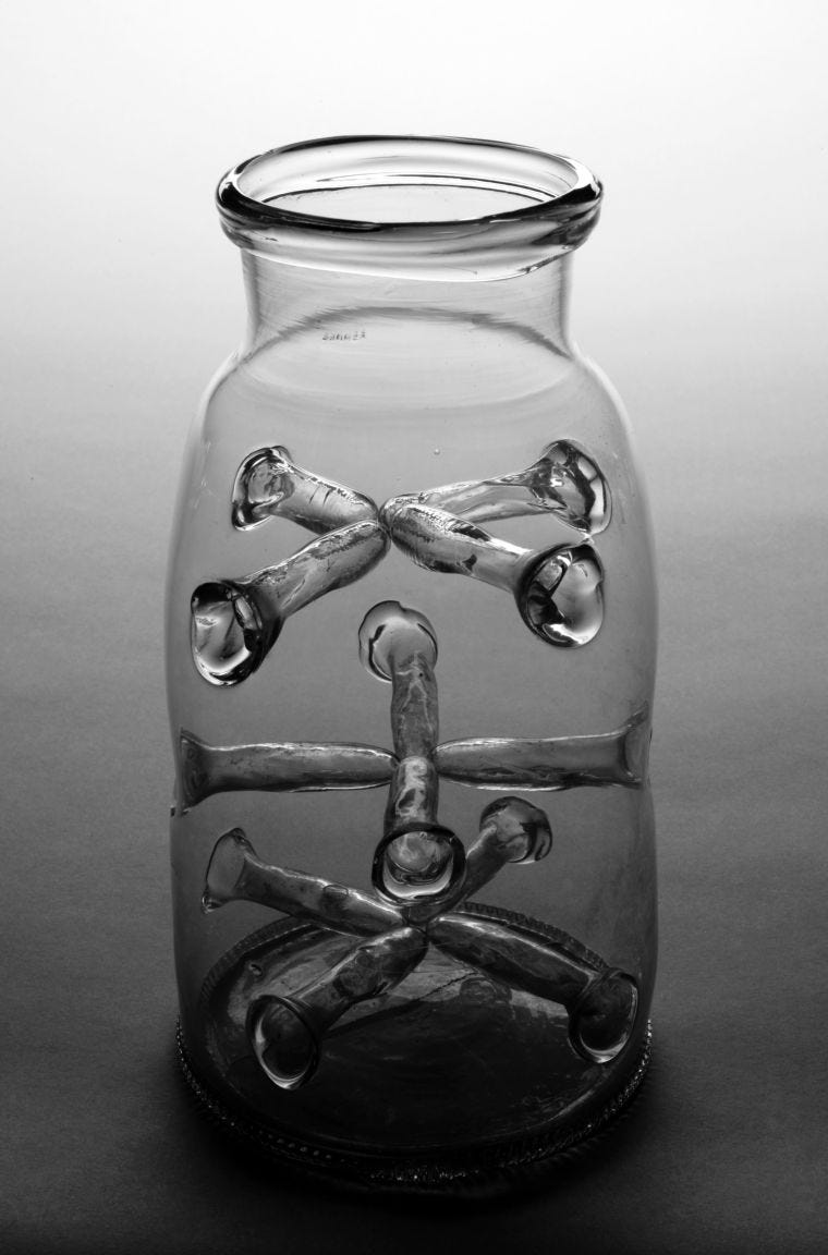 A photograph of a glass jar with 12 irregular-shaped glass tubes pointing inwards.