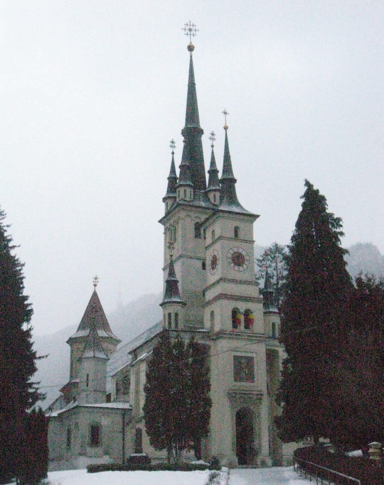 A white medieval church with black spires stands surrounded by trees in a snowy winter landscape.