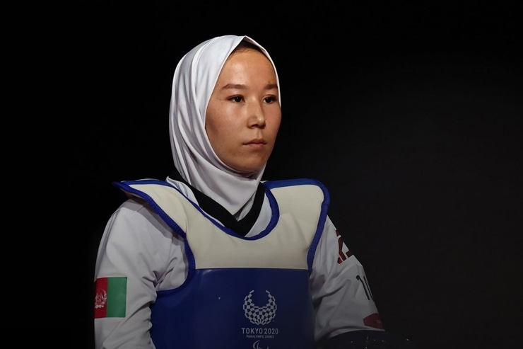 An Afghani woman has a serious and calm face, wearing a hijab and para taekwondo gear, facing to the right of the camera.