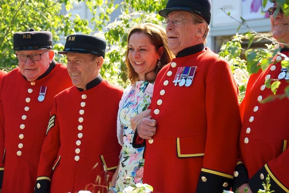 Smiling woman in floral dress with Chelsea Pensioners at the RHS Chelsea Flower Show