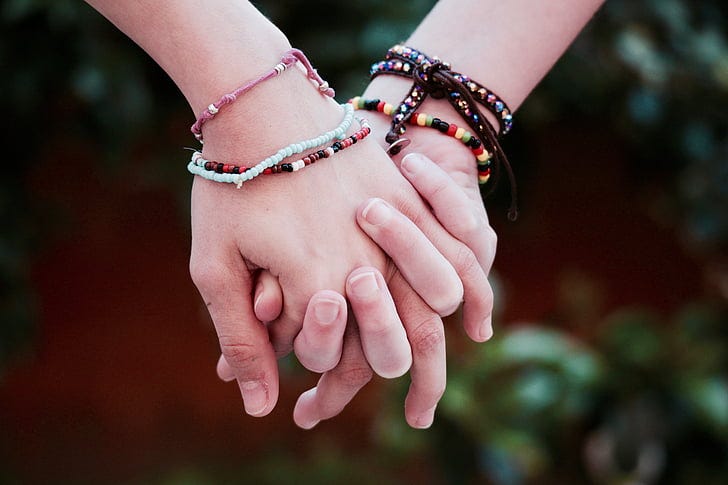 People holding hands wearing multi-colored friendship bracelets