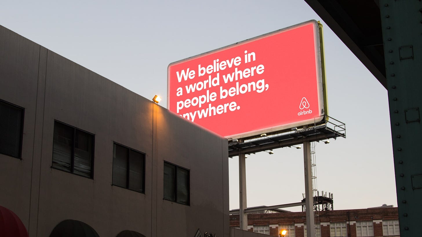 Airbnb billboard with text "We believe in a world where people belong, anywhere." against a pink background.