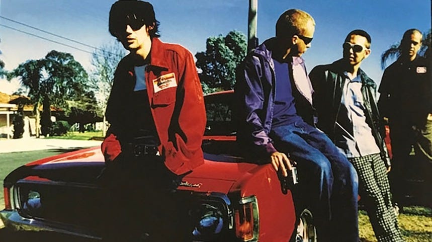 Four members of Grinspoon sitting on/standing around an old red car