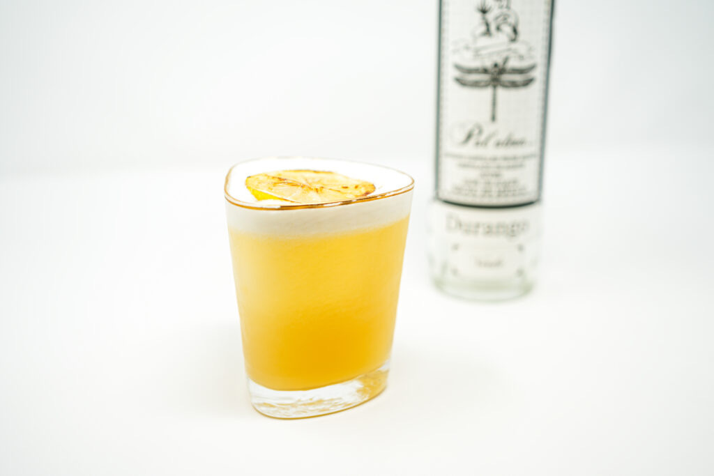 A frothy Limoncello Mezcal Sour served in a cocktail glass, garnished with a charred lemon slice, highlighting the smoky mezcal and tangy citrus flavors.