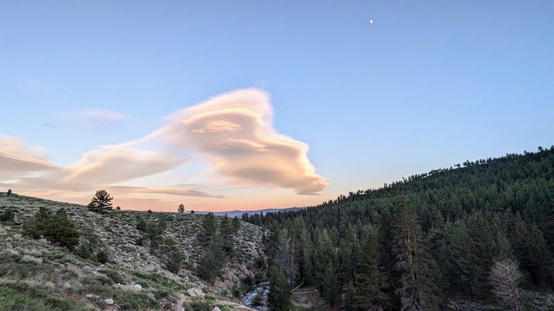 An interestingly curvy cloud in an otherwise clear sky, above mountains at dusk