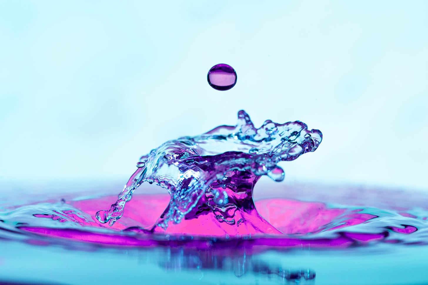 Foto de uma bolinha de gude lilás emergindo da água azul clara