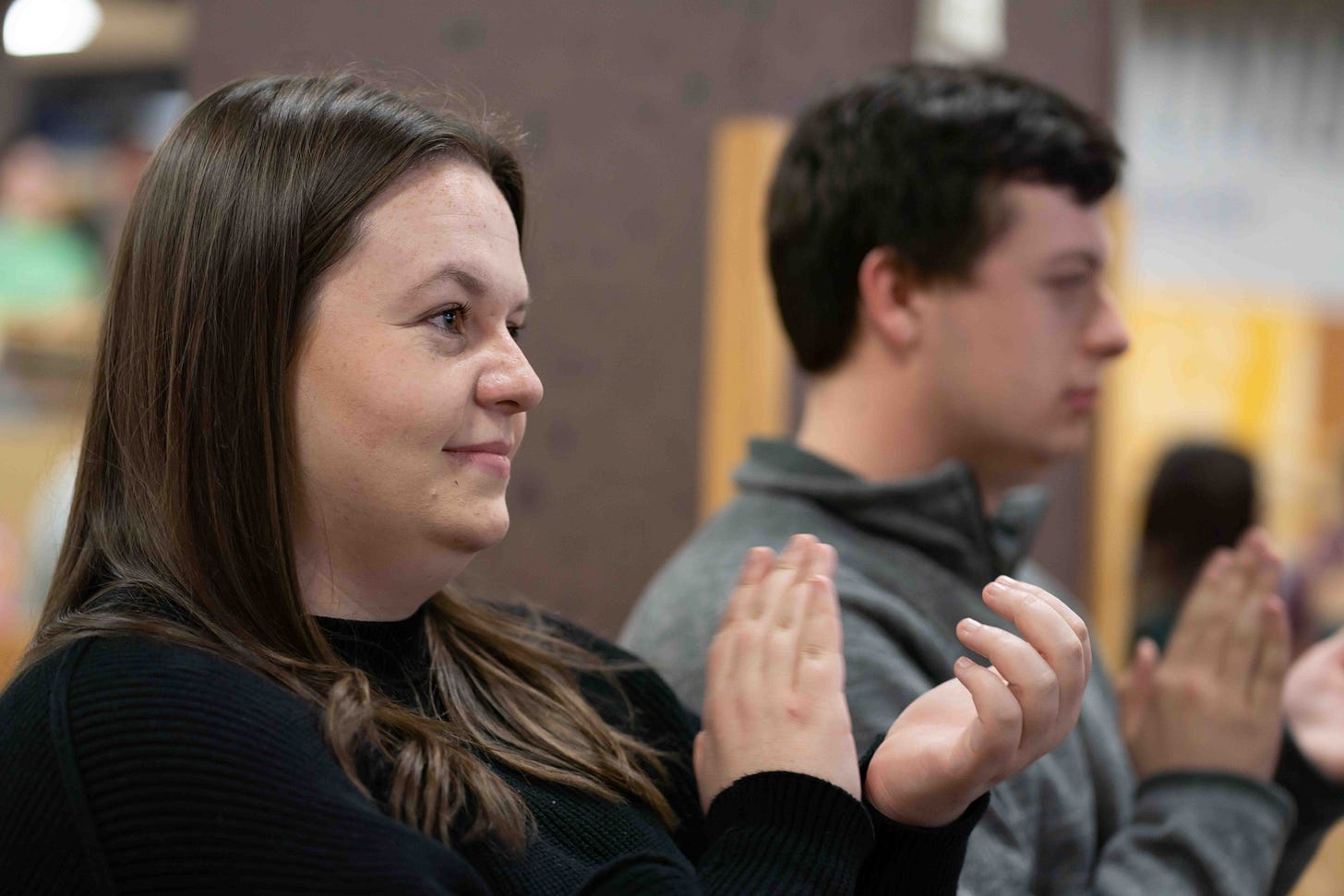 A young woman looks out of frame and claps.