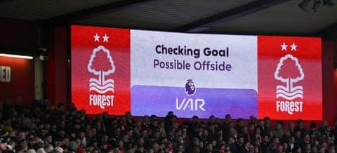 A crowd at a football match with 'Checking Goal – Possible Offside VAR' on a big screen behind them.
