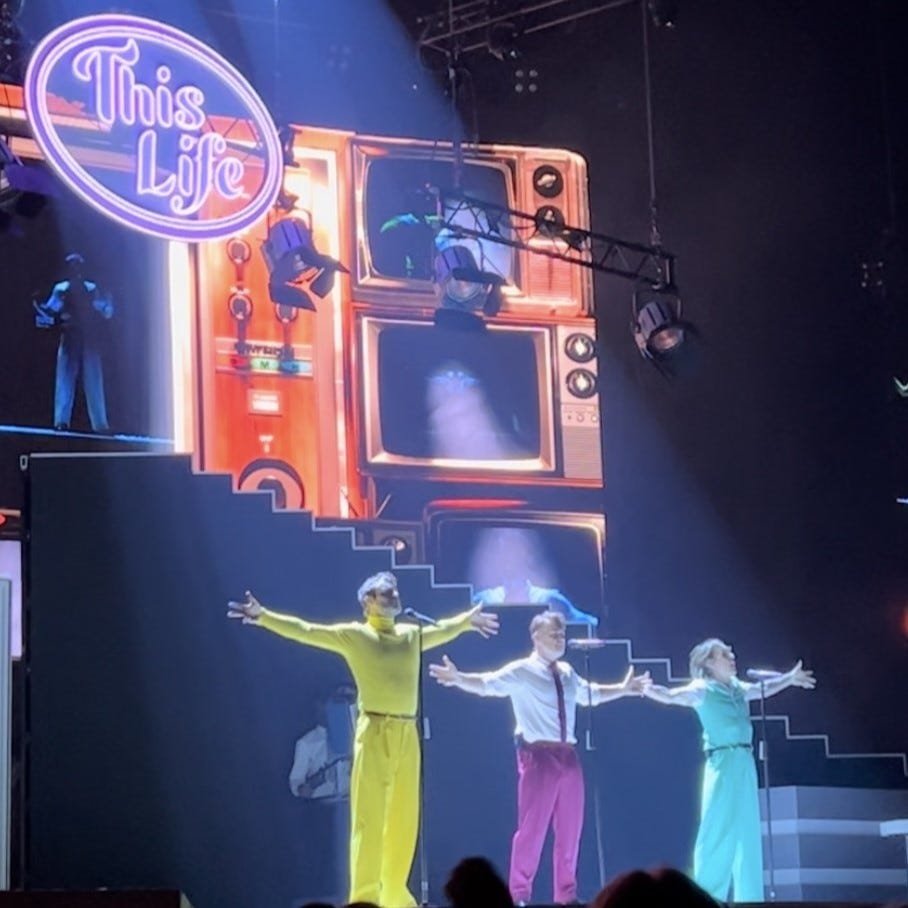 photo of the three take that boys on stage in bright suits with arms outstretched