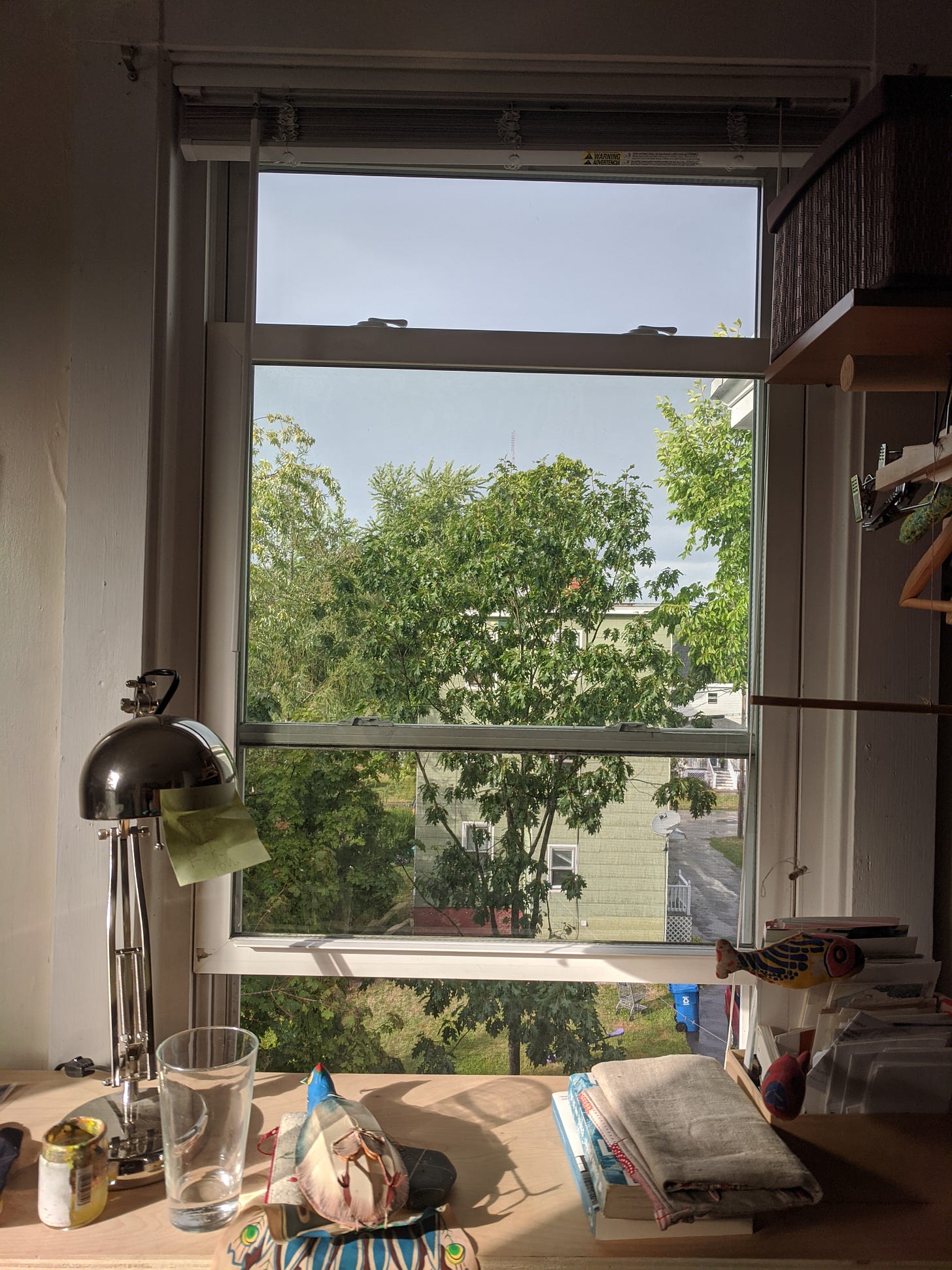 An open window in front of which there is a desk with bits and pieces of household things on it.
