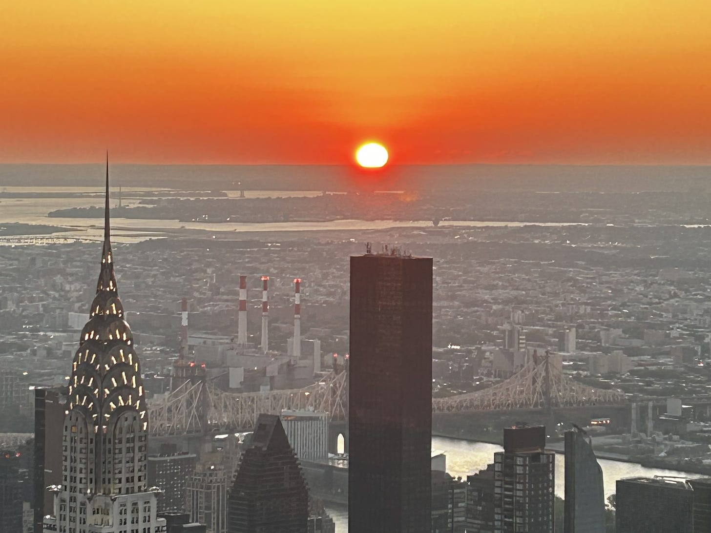View of new york skyline, from Empire state building, looking towards chrysler building and bridge with big orange sun rising in background