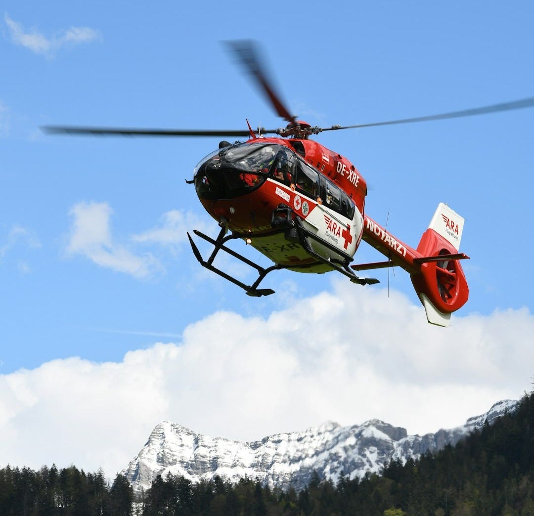 red and black helicopter flying over snow covered mountain during daytime