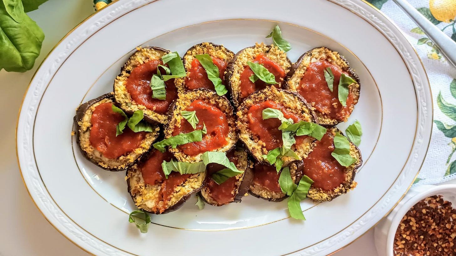 slices of breaded eggplant with tomato sauce and fresh basil leaves on plate.