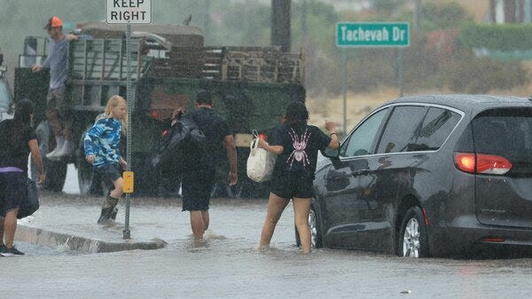People leave their cars on the road, walking through calf-deep water.