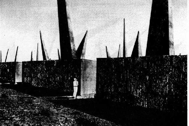 a black and white image of large blocks with gigantic spikes sticking out of them at different angles, and a human standing at the base looking into the ominous landscape beyond