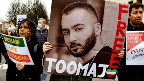 Getty Images A large placard of Toomaj Salehi's face and the words 'free Toomaj' is held up at a protest. He is a young man with a beard, and the photo is in black and white. Two protestors stand either side of the placard.