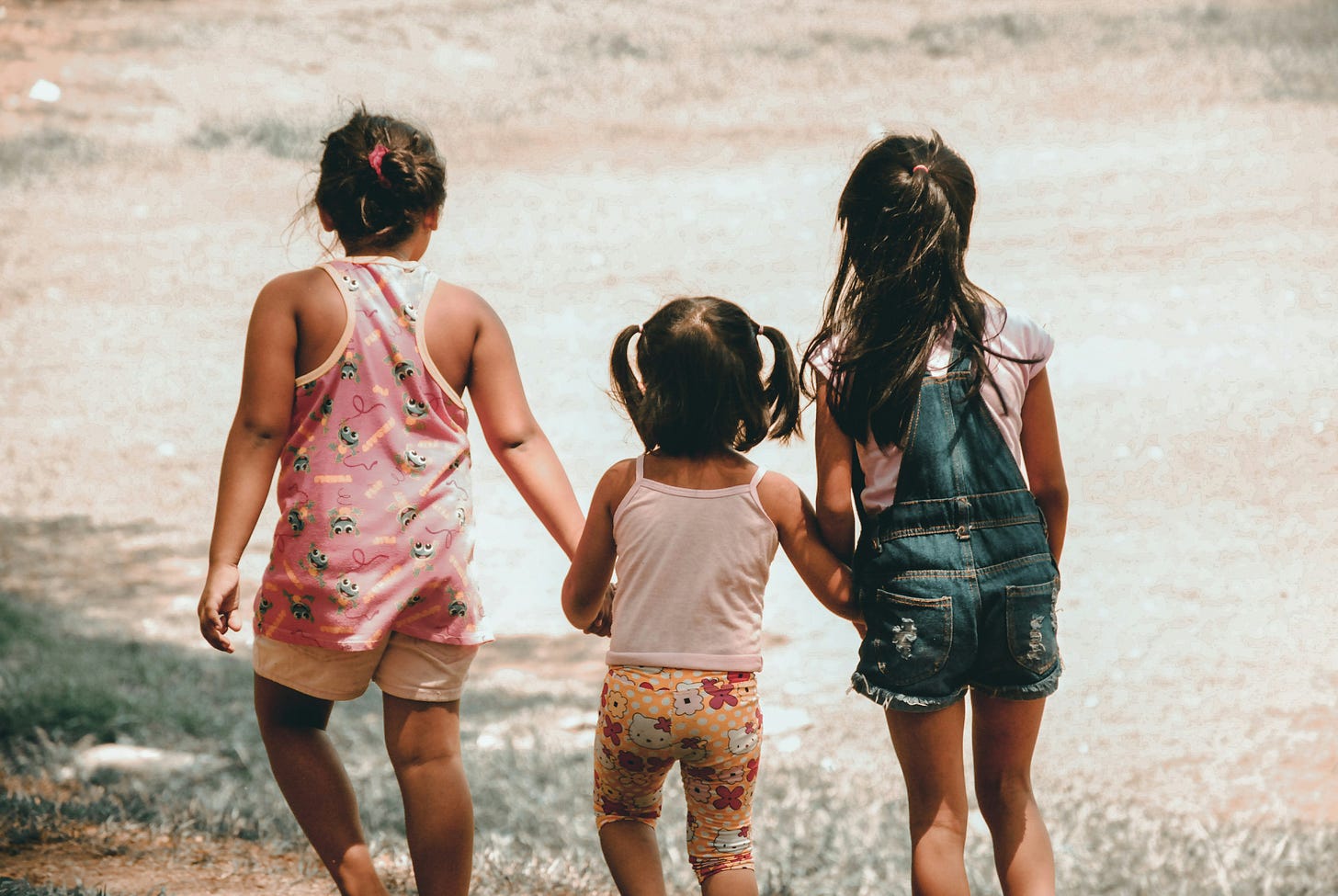 Tre bambine, viste di spalle, camminano su un sentiero tenendosi per mano