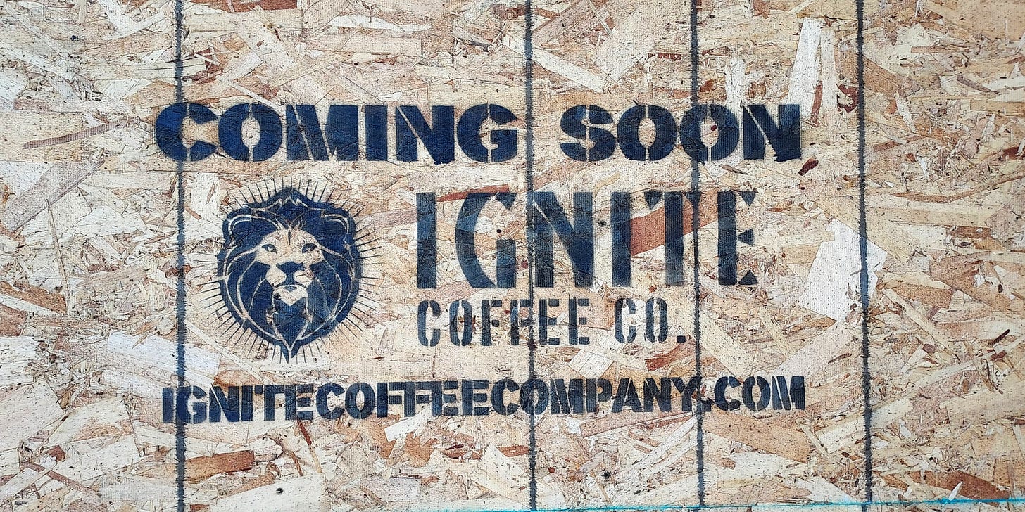 "Coming Soon. Ignite Coffee Co." is stenciled on a plywood sheet along with the company's lion head logo and website.