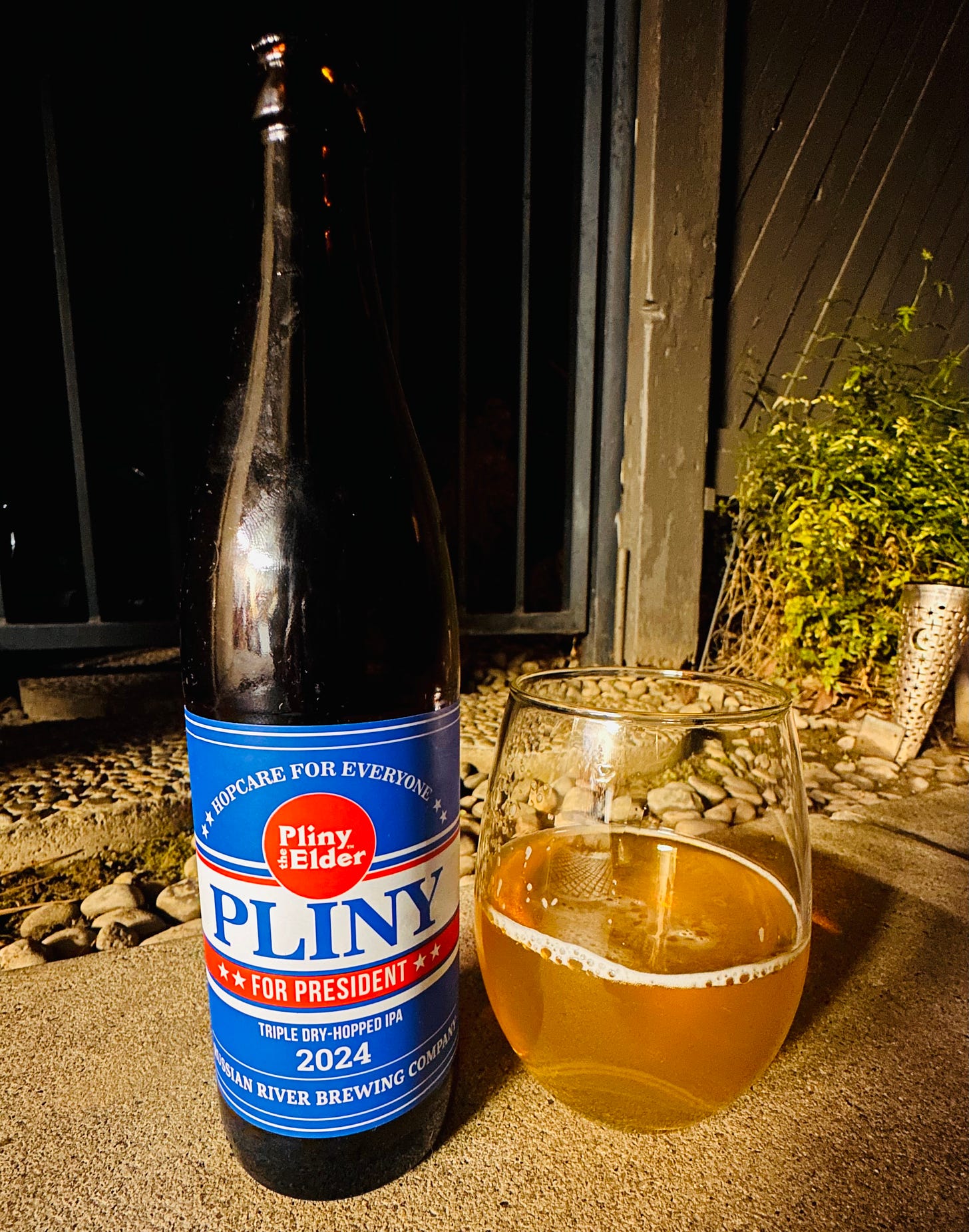 A bottle of Pliny For President beer 2024 next to a glass with the beer in it.