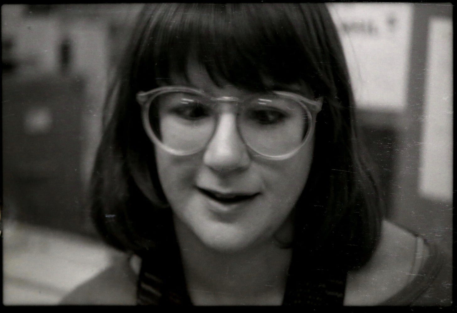 A black-and-white photo of a young, bespectacled woman with dark hair. Her lips are slightly parted as if she's in conversation.