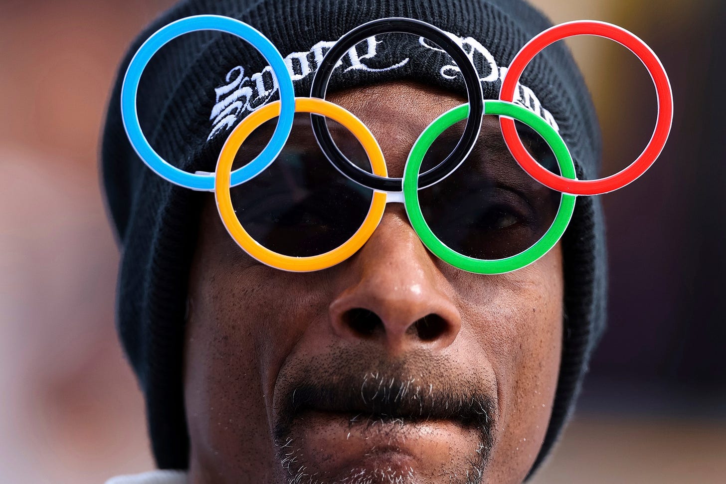 A closeup portrait of Snoop Dogg wearing a hat and Olympicring sunglasses during the 2024 Olympic Games in Paris.