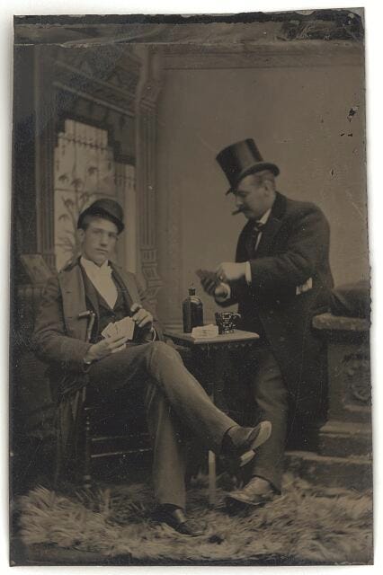 Photograph shows men wearing suits and top hats seated at a table playing cards; one man smokes a cigar. 