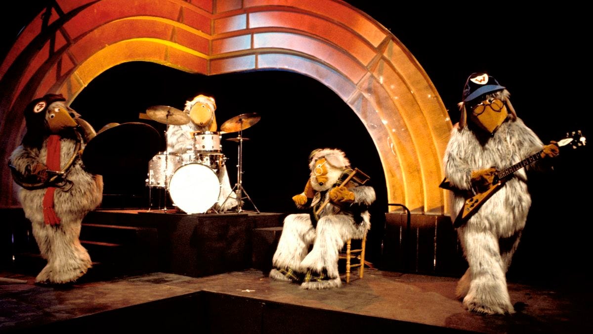 Wombles playing drums, big horn euphonium, thimble board and Flying V guitar on stage
