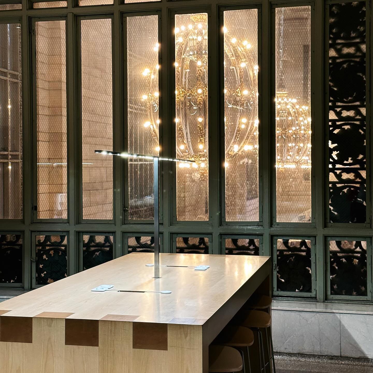 An empty table at Apple Grand Central. The station's ornate light fixtures glow through a window.