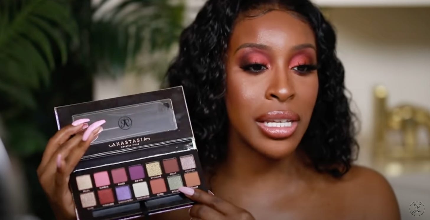 Influencer Jackie Aina holds up her Anastachia Beverly Hills collaboration palette, pointing at a dual-chrome green-brown shadow called sponsored