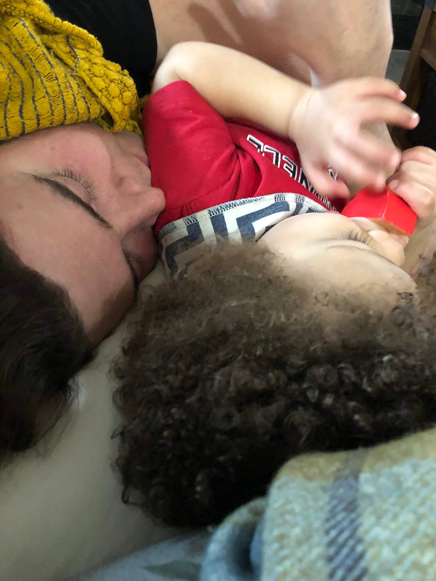 a white man with long hair snuggles his not-quite-two-year-old biracial child, who is wearing a Grinnell College shirt and blue-and-white bib