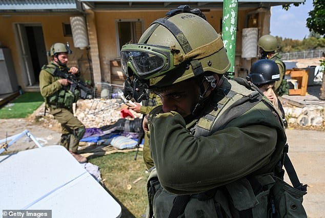An IDF Soldier covers his nose while walking past Hamas militants and Israeli civilians who were killed days earlier in an attack by Hamas militants on the Kfar Aza Kibbutz on Tuesday