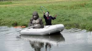 The actor Nick Mohammed attempts to get a hula hoop around a gorilla statue, which is floating on a raft in a small river. Nick is dressed as Dracula.